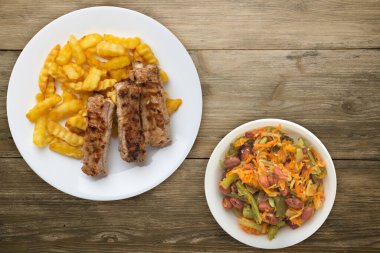 Beyaz tabakta domuz pirzolası ve patates, sebze salatası ve ahşap arka planda sos. Fast food 'un en iyi manzarası. Sağlıksız yiyecekler.