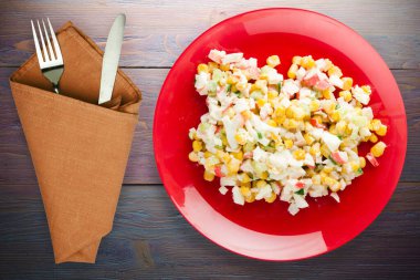 Çatal ve bıçak manzaralı kırmızı tabakta yengeç salatası. Mor ahşap arka planda yengeç salatası