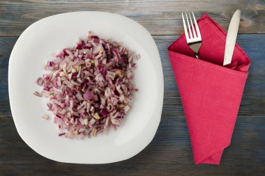 Mavi gri ahşap arka planda kırmızı soğan. Çatal ve bıçak manzaralı beyaz tabakta doğranmış kırmızı soğan.