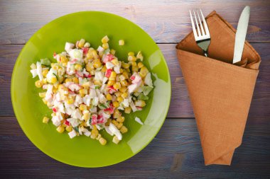 Kireç tabağında yengeç salatası, çatal ve bıçak manzaralı. Mor ahşap arka planda yengeç salatası