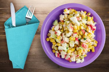 Mor tabakta çatal ve bıçak manzaralı yengeç salatası. Kahverengi ahşap arka planda yengeç salatası