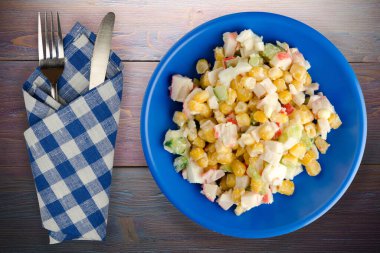 Çatal ve bıçak manzaralı lacivert tabakta yengeç salatası. Mor ahşap arka planda yengeç salatası