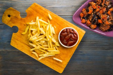 Gri mavi ahşap arka planda ketçaplı patates kızartması. Kahverengi ahşap tabakta patates kızartması ve vejetaryen salata.