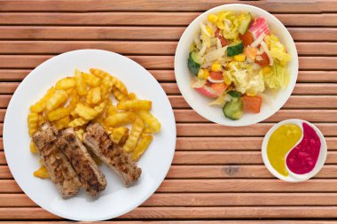 Beyaz tabakta domuz pirzolası ve patates, sebze salatası ve portakal ağacından arkaplanda sos. Fast food 'un en iyi manzarası. Sağlıksız yiyecekler.