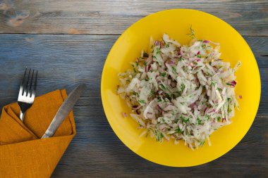 salata daikon, soğan ve dereotu mavi gri ahşap arka planda. Çatal ve bıçak manzaralı sarı tabakta salata.