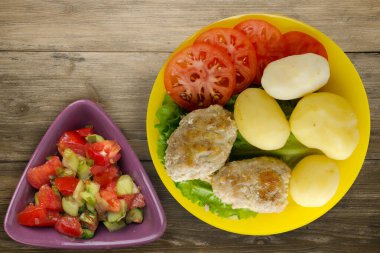 Sarı tabakta patates ve sebze salatası manzaralı pirzola. Kahverengi ahşap arka planda patatesli pirzola