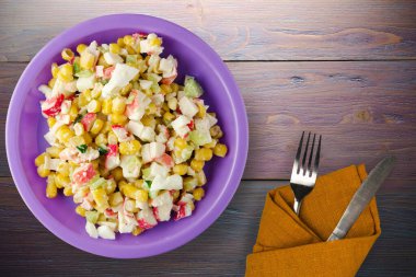 Mor tabakta çatal ve bıçak manzaralı yengeç salatası. Mor ahşap arka planda yengeç salatası