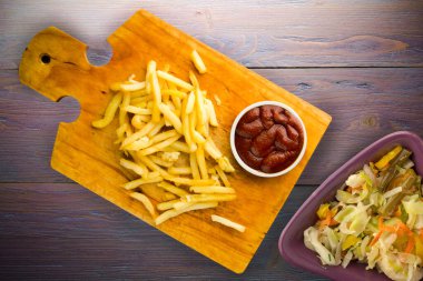 Patates kızartması ve mor ahşap arka planda ketçap. Kahverengi ahşap tabakta patates kızartması ve vejetaryen salata.