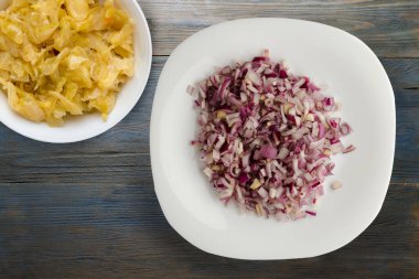 Mavi gri ahşap arka planda kırmızı soğan. Beyaz tabakta doğranmış kırmızı soğan ve vejetaryen salata.