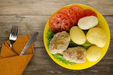 Çatal ve bıçak manzaralı sarı tabakta patatesli pirzola. Kahverengi ahşap arka planda patatesli pirzola
