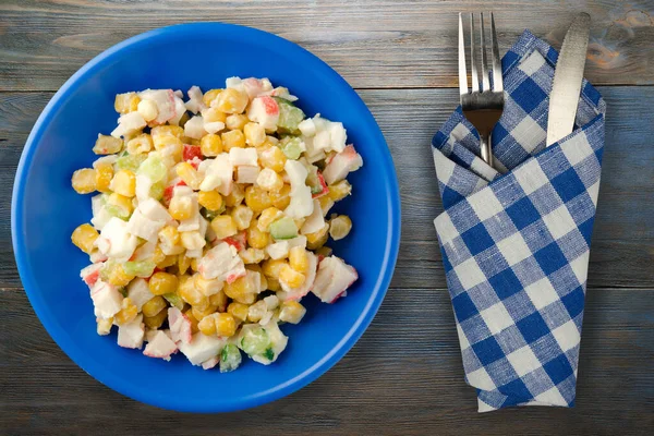 Çatal ve bıçak manzaralı lacivert tabakta yengeç salatası. Gri ve mavi ahşap arka planda yengeç salatası