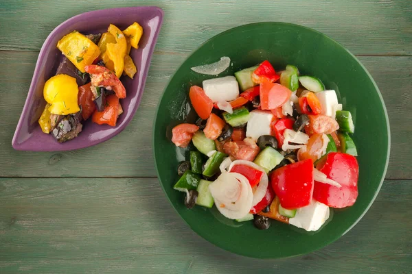 Yeşil ahşap arka planda Yunan salatası. Vejetaryen salata manzaralı yeşil tabakta Yunan salatası. sağlıklı yiyecekler