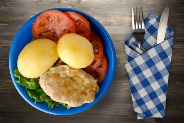  Çatal ve bıçak manzaralı mavi tabakta patatesli pirzola. Tahta arka planda patatesli pirzola.