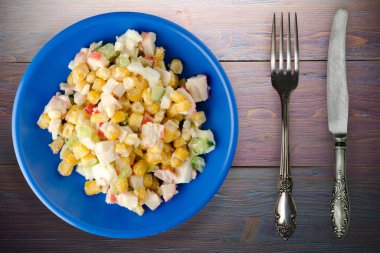 Çatal ve bıçak manzaralı lacivert tabakta yengeç salatası. Mor ahşap arka planda yengeç salatası