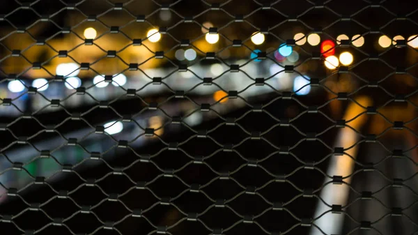 Blurred lighting of the city at night through fences — Stock Photo, Image