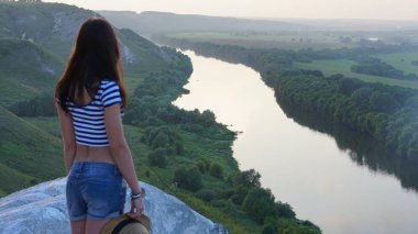 Kadın gezgin Kretase Dağı 'nın kıyısında duruyor ve nehir manzarasının keyfini çıkarıyor. Yaz günbatımı, Storozhevoe, Voronezh, Rusya.