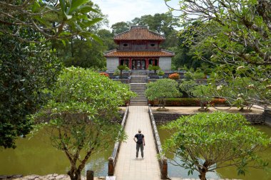 Hue Minh Mang Mezarı'nda Gezgin. Vietnam'da tatil. Popüler turistik gezi. Nehir ve taş köprü ile güzel bahçe.