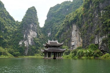 Nehirdeki küçük tapınak karst dağlarıyla çevrili. Trang 'da güzel manzara Tam Coc, Vietnam' da bir tekne turu.