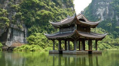 Nehirdeki küçük tapınak karst dağlarıyla çevrili. Trang 'da güzel manzara Tam Coc, Vietnam' da bir tekne turu.