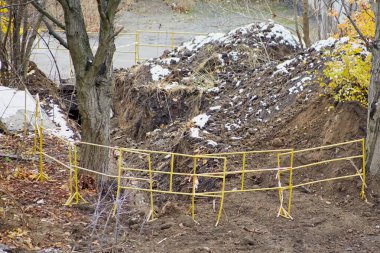 İnşaat bariyerleriyle çevrili derin kazılmış bir çukur, terk edilmiş bir çukur, derin bir deliği olan bir inşaat sahasında çit..