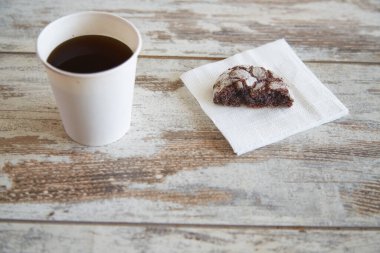 Çikolatalı kurabiyenin yarısının olduğu bir kağıt peçete ve yanında bir bardak kahve, ahşap bir masanın üzerinde, yakın plan, yarım porsiyon, sağlıklı kahvaltı, tatlı ve hamur işi tüketimini sınırlandıran. 