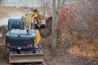 The excavator is digging a deep pit on a construction site in a natural environment.