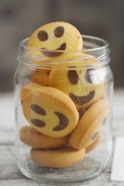 Cam kavanozdaki kurabiyeler masanın üzerinde gülümseyen emojiler şeklinde dikey çekim.