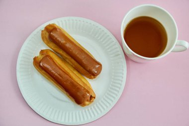 İki Claire, beyaz bir tabakta pembe bir arka planda bir fincan çayın yanında yatıyorlar.