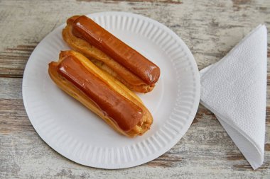 İki Clair, beyaz bir kağıt tabakta, tahta bir masanın üzerinde, kağıt peçetenin yanında, yakın plan.