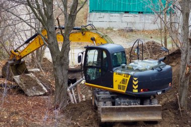 A backhoe loader lifting a concrete slab during the repair of a water pipeline, backhoe loader in municipal repair work, aging pipeline accident.