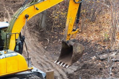 Close-up of a backhoe excavator bucket above a new construction site, developing a new construction area, excavator operation for cleanup in construction, various tasks for excavators.