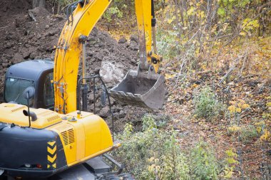 The excavator with a raised bucket above the dug soil on the construction site.