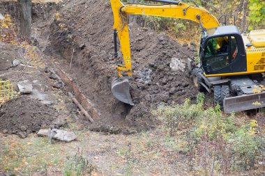 The excavator digs a pit and dumps soil on a construction site in a natural environment.