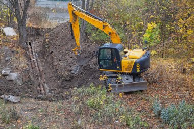The working process of an excavator: the bucket scoops soil against a background of greenery.