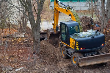 A construction excavator digs a trench among trees in a natural setting.