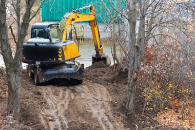 The excavator is digging the soil at a new construction site, the excavator is digging the soil in an area with trees, excavator operation in construction.