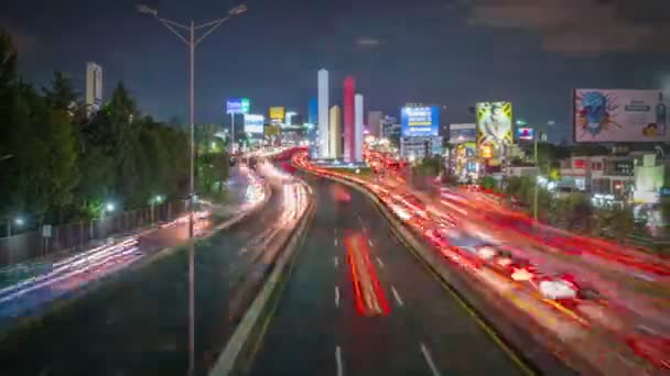 Hyperlapse atemberaubende Nachtsicht auf eine riesige Autobahn. Viele rot-weiße Autolichter erhellen die Nacht. im hinteren bereich türmt sich das Wahrzeichen von Mexiko-Stadt auf.