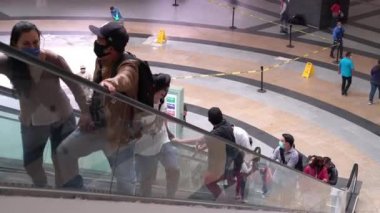 İnsanlar elektrikli merdivenlerde maske takıyor.