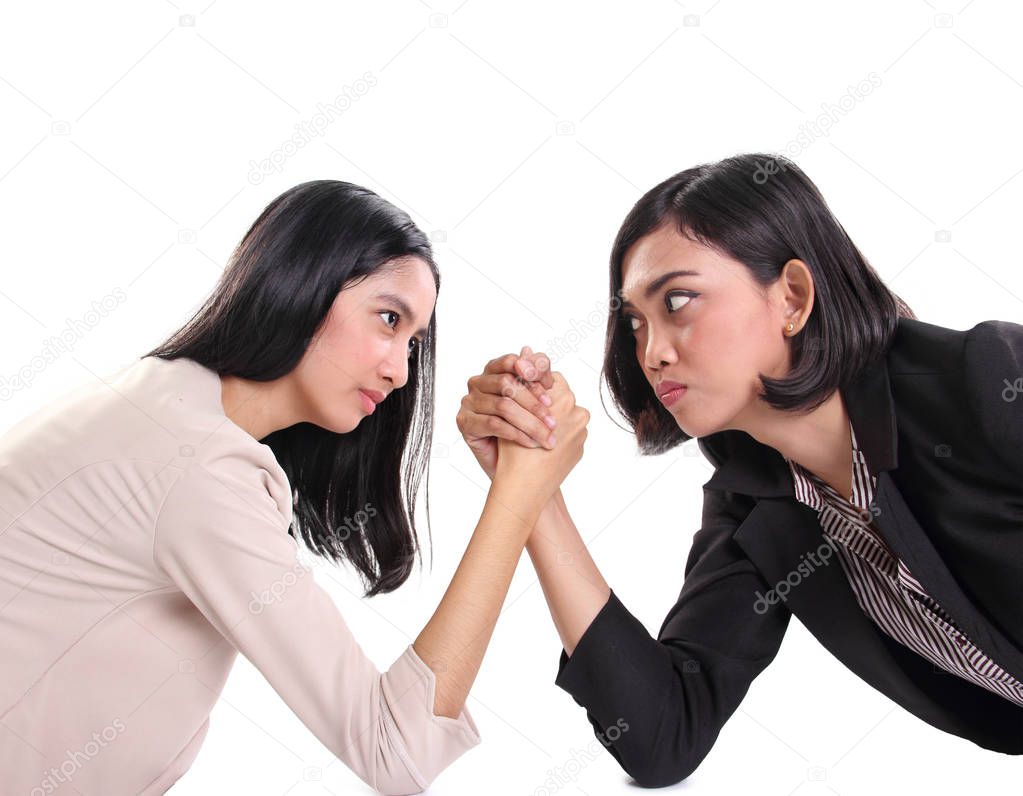Two female business workers stare against each other with serious faces, compete in arm wrestling. Side portrait, isolated over white background