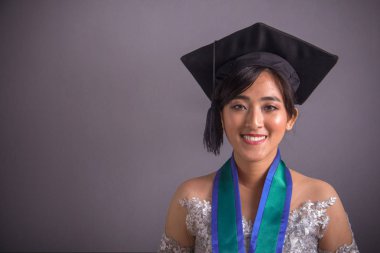 Kamera için gri arka plan üzerinde gülümseyen mezun Güneydoğu Asya kız öğrenci portresi kapatın