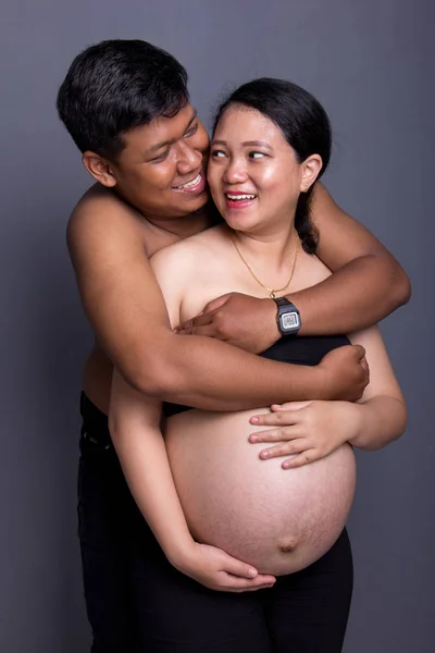 Graviditet par omfamna och leende till varandra, på grå — Stockfoto