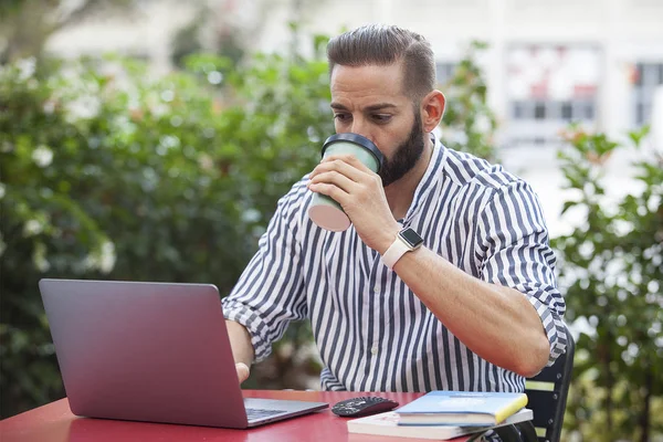 Entrepreneur man drinking and working with a laptop in a bar terrace