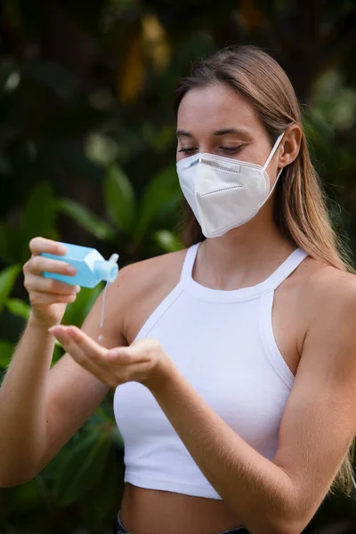Covid-19- Woman wearing a mask  and washing her hands with clear alcohol gel bottle to prevent the spreading of the corona virus