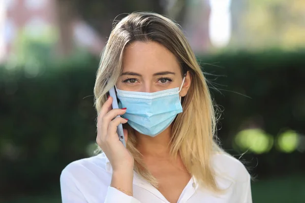 Tıbbi maske takan ve cep telefonuyla konuşan virüsten korunan beyaz bir kadın. 