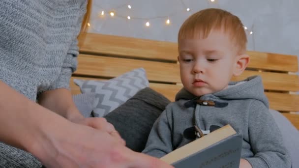 Junge Mutter und ihr kleiner Sohn lesen zu Hause Buch — Stockvideo