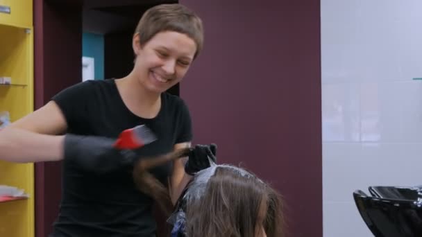Профессиональный парикмахер раскрашивает волосы женщины-клиента в студии — стоковое видео