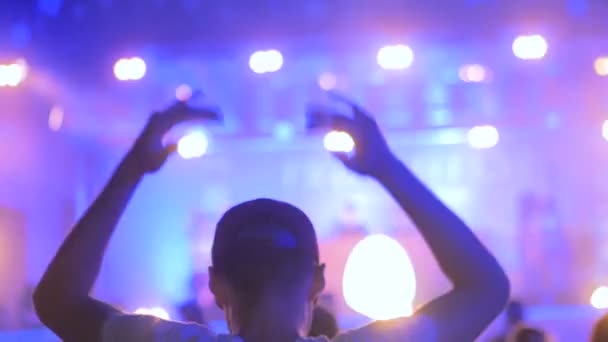 Мужской силуэт тусуется ночью на концерте под открытым небом перед сценой — стоковое видео