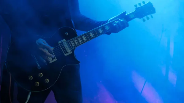 Close up shot of man playing guitar on concert stage. Smoke, blue light. Entertainment and art concept