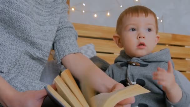 Dois tiros. Jovem mãe e seu filho bebê lendo livro em casa — Vídeo de Stock