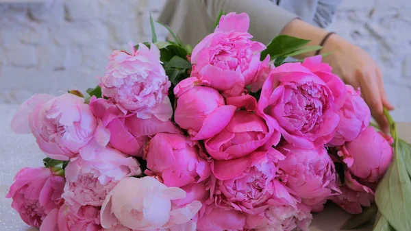 Professional woman floral artist, florist making bunch of pink peonies at workshop, flower shop. Floristry, handmade and small business concept